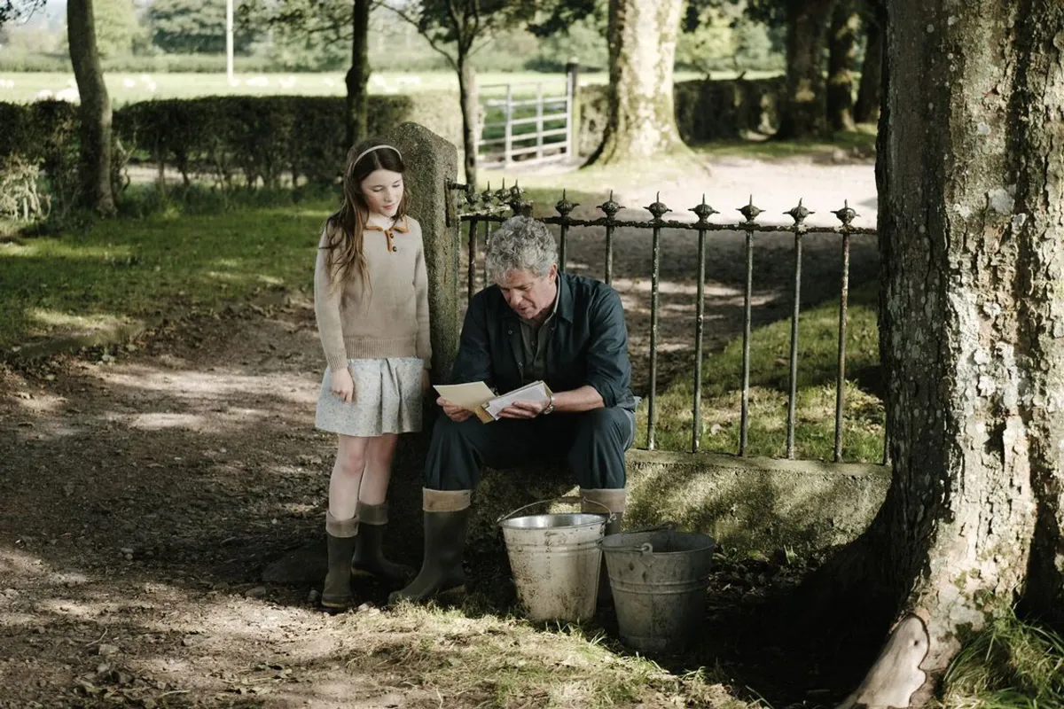 A young girl watches on as a man reads a letter in a rural scene (from the film An Cailín Ciúin)
